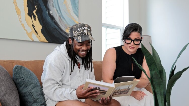 A couple relaxes on the couch reading in the living room of a staged CLT home at 2080 Union.